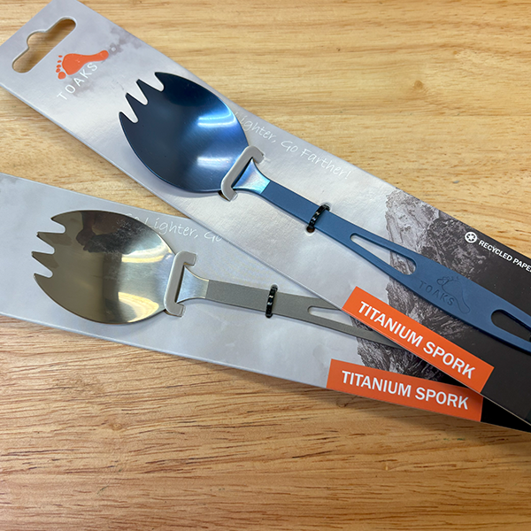 Two titanium sporks in packaging on a wooden surface